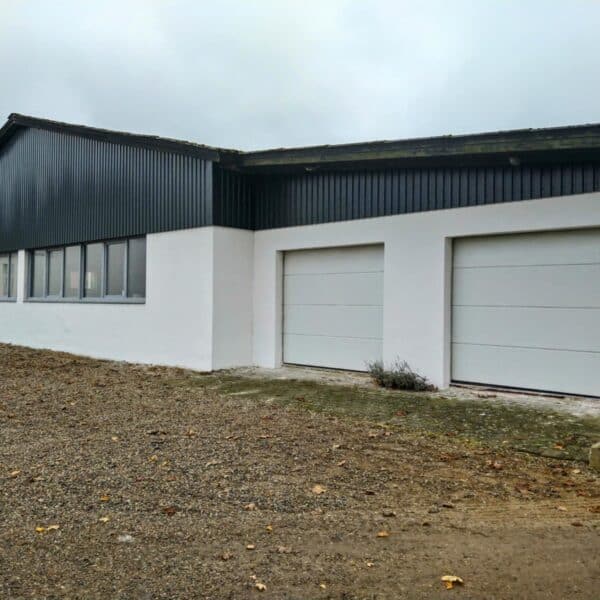 Nærbillede af en renoveret facade i Brørup med armeringspuds, hvor detaljer som garageporte og sorte facadepaneler er fremhævet. Bygningen fremstår robust og æstetisk opdateret.